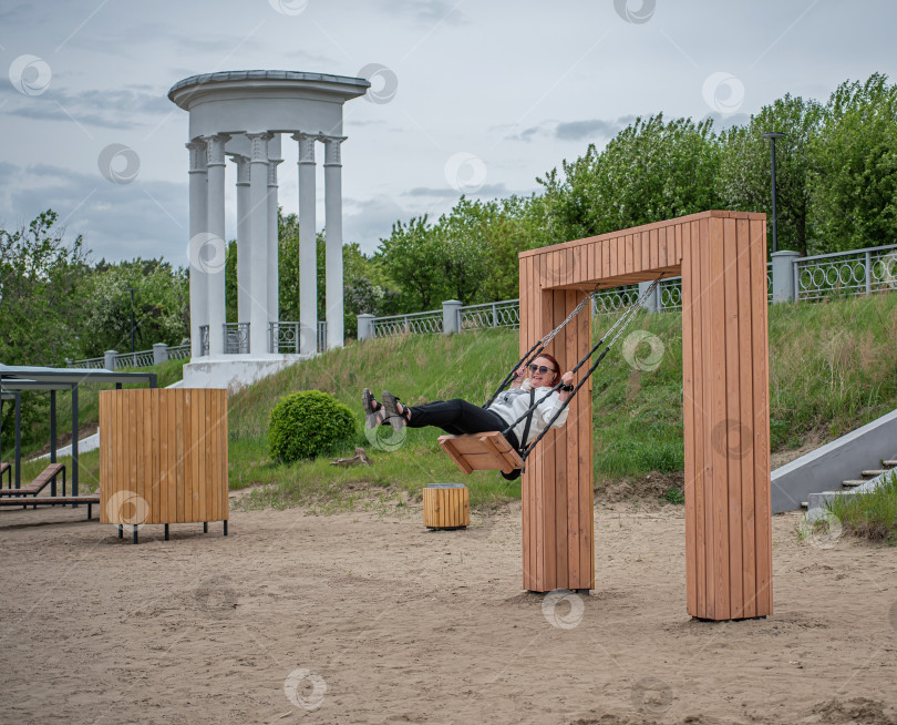 Скачать Россия,город Железногорск Красноярский Край, 25 мая 2025 год.Девушка качается на подвесных  качелях . Вокруг деревья и зелень. фотосток Ozero