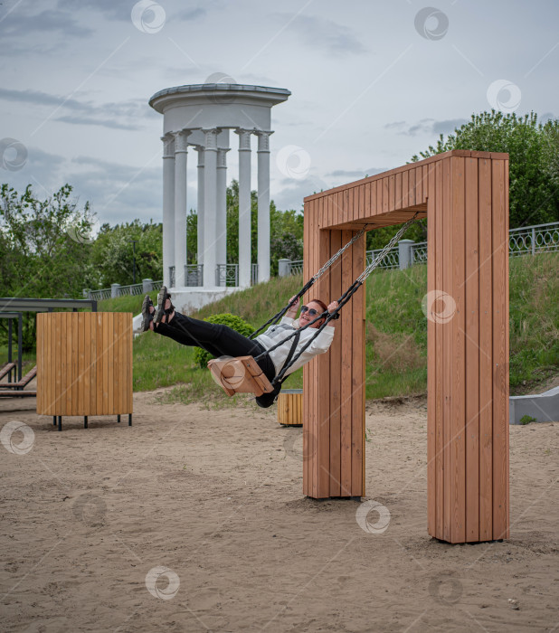 Скачать Россия,город Железногорск Красноярский Край, 25 мая 2025 год.Девушка качается на подвесных  качелях . Вокруг деревья и зелень. фотосток Ozero