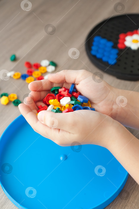 Скачать Детские руки складывают детали цветной мозаики в рисунок цветов на столе. Досуг ребенка в заключении. Настольная игра. Вид сверху фотосток Ozero
