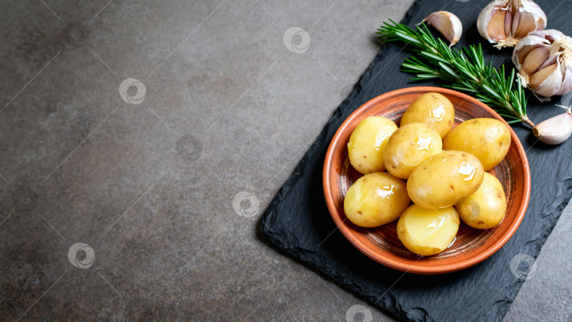 Скачать Готовый картофель в миске с розмарином и чесноком на чёрном каменной каменной доске фотосток Ozero