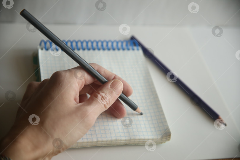 Скачать Женщина левша пишет карандашом в блокноте в клетку на столе крупным планом фотосток Ozero