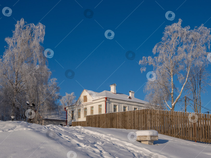 Скачать Солнечный снежный пейзаж с белым домом за деревянным забором.. фотосток Ozero