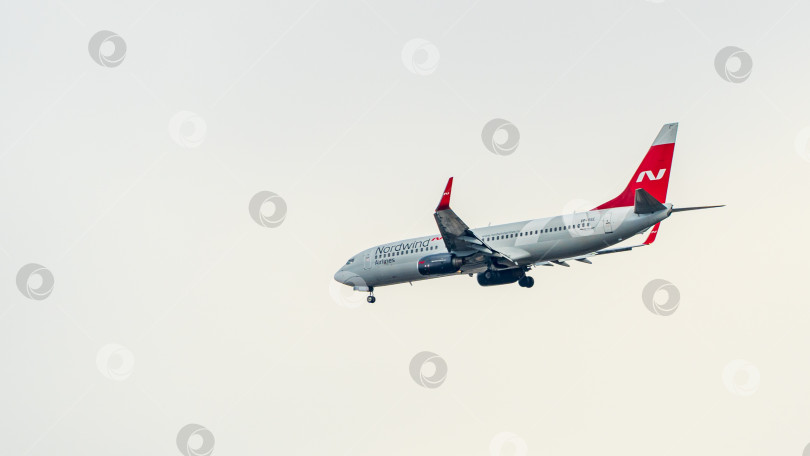 Скачать Boeing 737-800 авиакомпании Nordwind Airlines летит со снижением к взлетно-посадочной полосе на фоне облачного неба. Крупный план. Шасси и закрылки самолета выпущены. фотосток Ozero