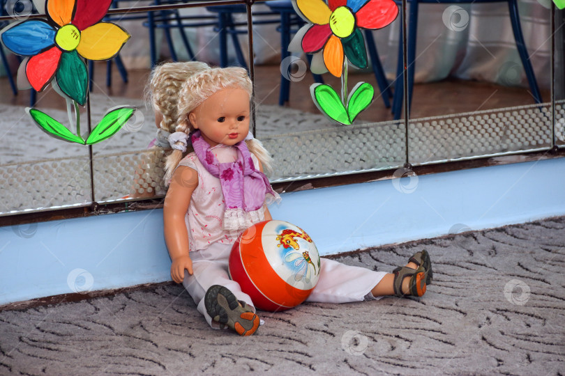 Скачать Игрушечная кукла с мячом сидит у зеркала на полу в детском саду. Концепция одиночества и ожидания фотосток Ozero