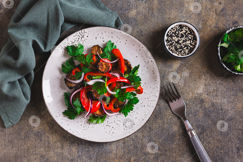 Скачать Теплый салат с обжаренными баклажанами, болгарским перцем, луком и зеленью на тарелке на столе вид сверху фотосток Ozero