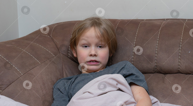 Скачать Больной мальчик лежит на коричневом диване под одеялом. Уставший ребенок отдыхает дома с симптомами гриппа. Больной ребенок выздоравливает после болезни фотосток Ozero