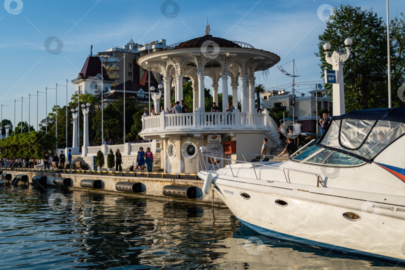 Скачать Сочинский морской торговый порт на закате. Теплоходы и яхты у причала перед главным зданием Морского вокзала. Крупный план. Спокойное Черное море. Отражение яхт в воде. фотосток Ozero