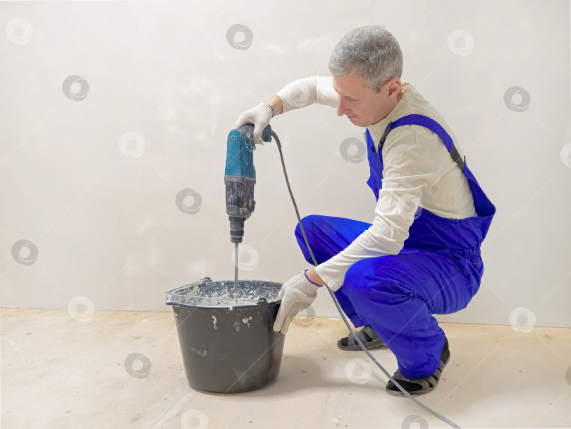 Скачать Видно, как рабочий в синем комбинезоне замешивает жидкий бетон в помещении фотосток Ozero