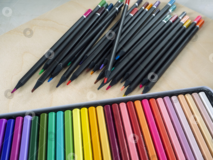Скачать Цветные художественные карандаши для художников, творчества и хобби. Цветные карандаши аккуратно разложены в открытой коробке, а набор карандашей разложен на деревянной поверхности. фотосток Ozero