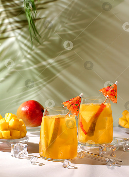 Скачать Домашний коктейль, сок или лимонад с кусочками манго и льдом на залитом солнцем кухонном столе. Концепция летней вечеринки. Рецепт освежающего летнего диетического напитка, детокс-диета и здоровый образ жизни фотосток Ozero