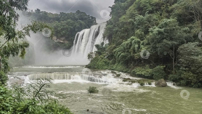 Скачать Красивый тропический водопад. Потоки белой воды стекают со скалы в реку. фотосток Ozero