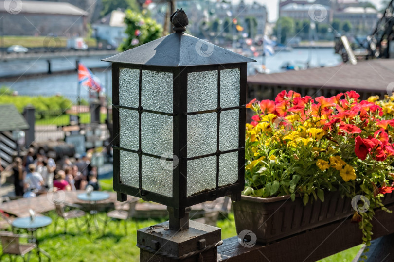Скачать Яркий цветочный ящик рядом с фонарем с видом на людей и лодки у воды на оживленной открытой площадке в течение дня фотосток Ozero