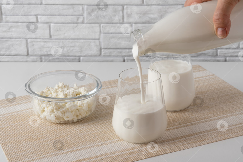 Скачать Заливка из домашнего кефира, пахты или йогурта с пробиотиками. Йогурт течет из стеклянной бутылки на светлом фоне. Холодный кисломолочный напиток с пробиотиками. Модные блюда и напитки фотосток Ozero