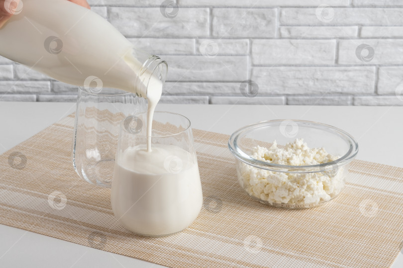Скачать Заливка из домашнего кефира, пахты или йогурта с пробиотиками. Йогурт течет из стеклянной бутылки на светлом фоне. Холодный кисломолочный напиток с пробиотиками. Модные блюда и напитки фотосток Ozero