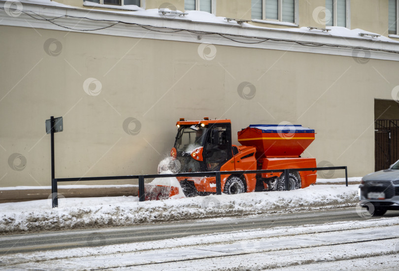 Скачать Компактная универсальная машина для уборки городских улиц очищает тротуары от снега. На фоне зимнего города. Пермь, Пермский край, Россия. 02.2026 фотосток Ozero