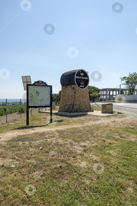 Скачать 24 августа 2025 года: Жанровая скульптура в виде бочки с вывеской винодельни в Мысхако, Россия, на фоне моря и гор на горизонте, символизирующая местное виноделие, туризм и прибрежный ландшафт. фотосток Ozero