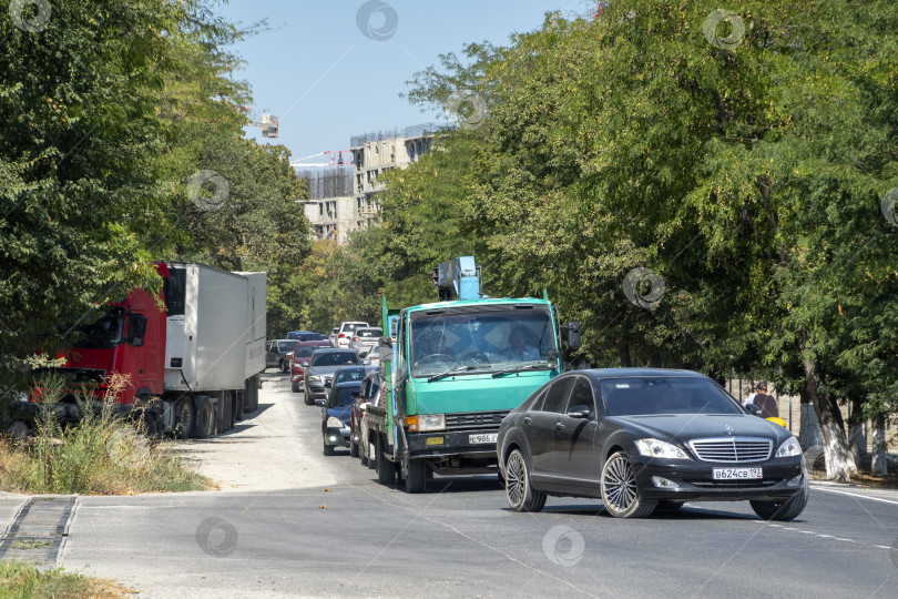 Скачать 24 августа 2025 года: Дорога из Мысхако в Новороссийск с деревьями по обочинам, проезжающими машинами и открытым небом, представляющая повседневные путешествия, транспорт и пригородный пейзаж. фотосток Ozero