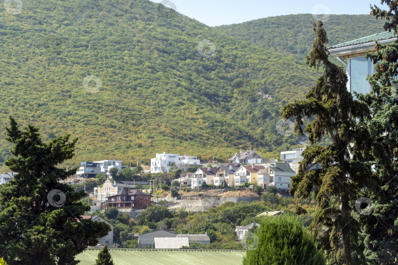 Скачать Городская дорога в Мысхако, Россия, с автомобилями и жилыми домами, горами и морем на заднем плане, показывающая повседневную жизнь и прибрежный городской пейзаж. фотосток Ozero