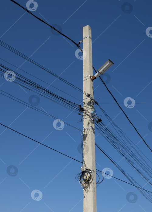 Скачать Бетонный столб уличного освещения с многочисленными электрическими проводами на фоне ясного голубого неба, символизирующий городскую инфраструктуру, электрические сети и городскую среду фотосток Ozero