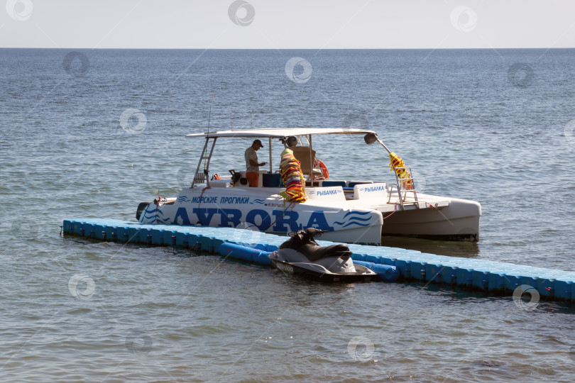 Скачать 24 августа 2025 года: Пирс в Мысхако, Россия, с водным мотоциклом и большим морским катамараном, пришвартованными неподалеку, демонстрирует береговую инфраструктуру, морской транспорт и летние развлечения на море. фотосток Ozero