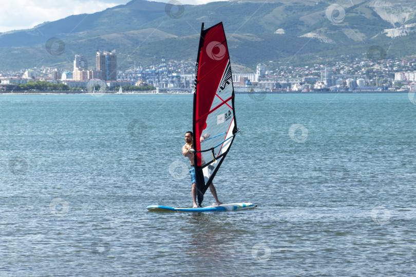 Скачать 24 августа 2025 года: Спортсмен занимается виндсерфингом в море недалеко от Новороссийска, Россия, с парусной доской и волнами, демонстрируя водные виды спорта, активный образ жизни и отдых на побережье. фотосток Ozero