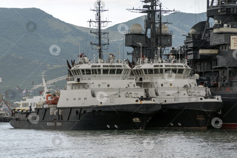 Скачать 24 августа 2025 года: Спасательные суда пришвартовались в порту Новороссийска, Россия, на фоне гор, иллюстрирующих безопасность на море, портовые операции и деятельность на побережье Черного моря. фотосток Ozero