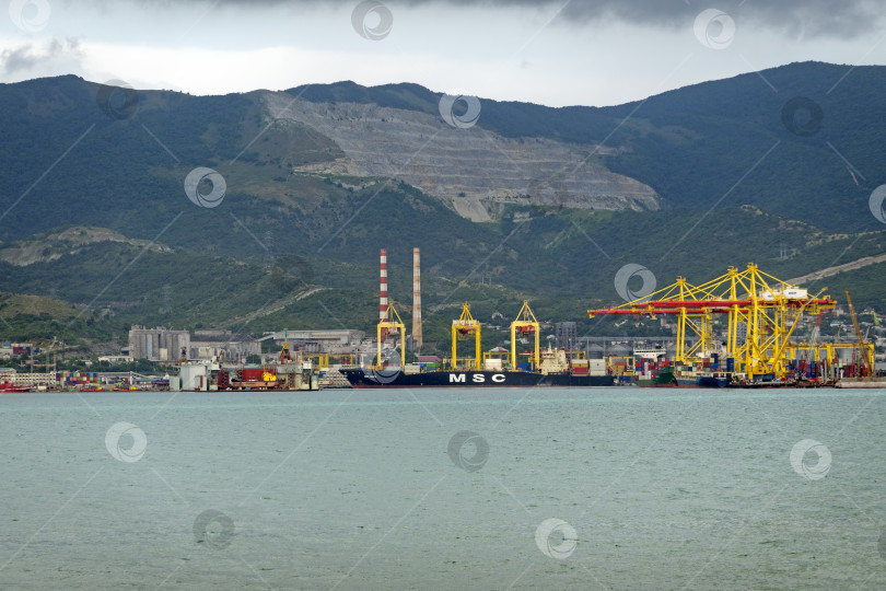 Скачать 22 августа 2025 года, вид порта Новороссийск, Россия, с грузовыми судами и кранами на побережье. Промышленный морской пейзаж на Черном море фотосток Ozero