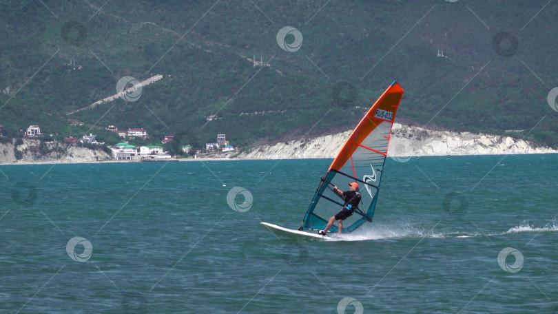 Скачать 24 августа 2025 года: Спортсмен занимается виндсерфингом в море недалеко от Новороссийска, Россия, с парусной доской и волнами, демонстрируя водные виды спорта, активный образ жизни и отдых на побережье. фотосток Ozero