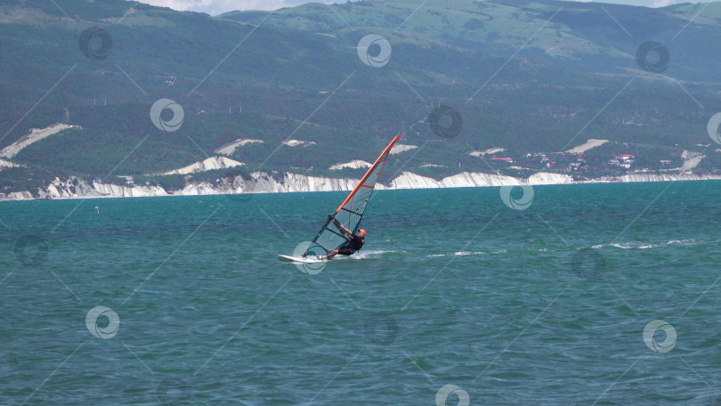 Скачать 24 августа 2025 года: Спортсмен занимается виндсерфингом в море недалеко от Новороссийска, Россия, с парусной доской и волнами, демонстрируя водные виды спорта, активный образ жизни и отдых на побережье. фотосток Ozero
