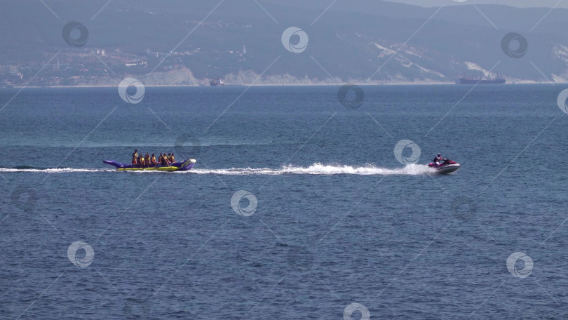 Скачать 24 августа 2025 года: Гидроцикл буксирует надувной банан по морю в Мысхако, Россия, демонстрируя пляжные развлечения, водные виды спорта и летний отдых на побережье. фотосток Ozero