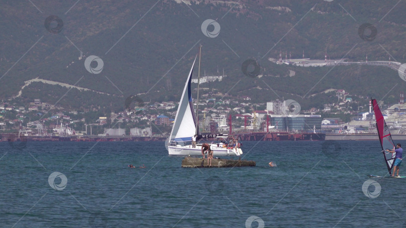 Скачать 24 августа 2025 года: Спортсмен занимается виндсерфингом в море недалеко от Новороссийска, Россия, с парусной доской и волнами, демонстрируя водные виды спорта, активный образ жизни и отдых на побережье. фотосток Ozero