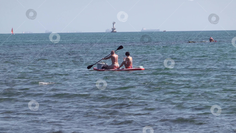 Скачать 23 августа 2025 года, Россия, Новороссийск. Мужчина и женщина плывут по морю на SUP-доске, наслаждаясь летними приключениями и живописными видами побережья. фотосток Ozero