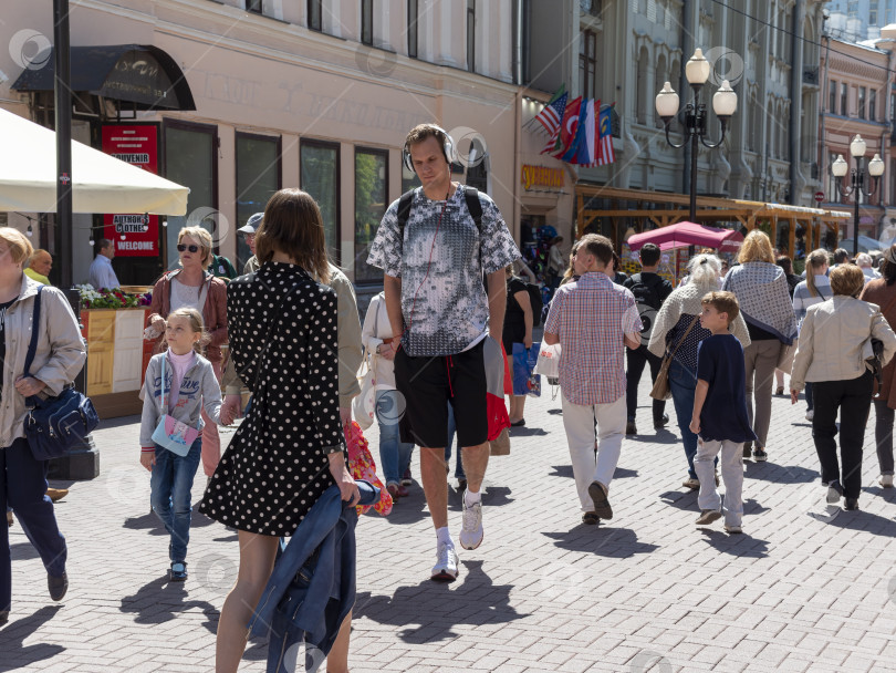 Скачать 14 июля 2022 года: Высокий баскетболист прогуливается по Старому Арбату в Москве, Россия, в наушниках, представляя городской образ жизни, спортивную культуру и повседневную городскую жизнь фотосток Ozero