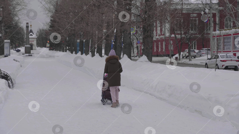 Скачать 28 декабря 2025 года, Барнаул, Россия. Женщина с ребенком прогуливается зимой по аллее центрального парка, наслаждаясь катанием на санках, снежным пейзажем и городским отдыхом на свежем воздухе. фотосток Ozero