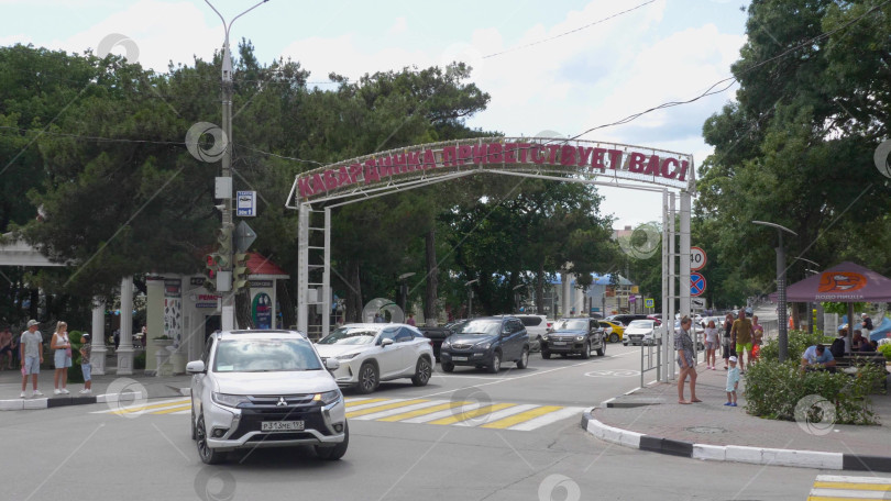 Скачать 24 августа 2025 года: Входная арка рядом с автобусной станцией в центре села Кабардинка, Россия, с табличкой "Кабардинка приветствует вас", представляющей достопримечательность села и местные пейзажи. фотосток Ozero