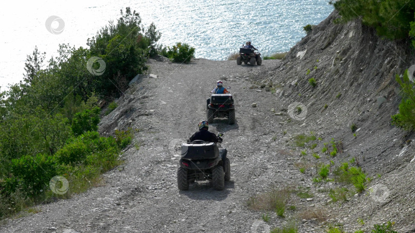 Скачать 23 августа 2025 года, Россия, Новороссийск. Гонщики на квадроциклах едут по грунтовой дороге вдоль моря, наслаждаясь приключениями и живописными видами побережья под ясным небом. фотосток Ozero