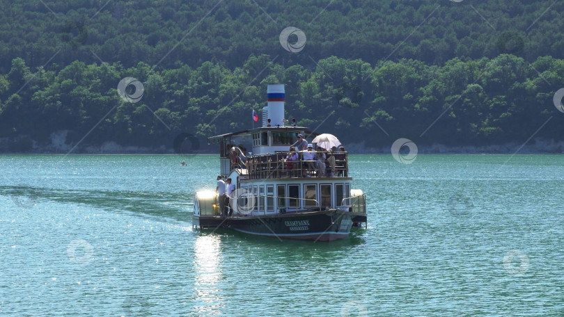 Скачать 19 августа 2025 года пассажирский теплоход "Шампань" причаливает к берегу озера Абрау-Дюрсо, окруженного спокойной водой и живописным ландшафтом фотосток Ozero