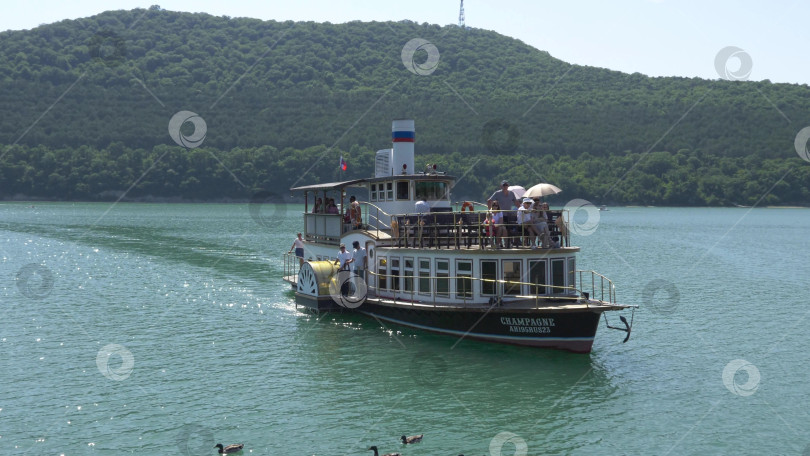 Скачать 19 августа 2025 года пассажирский теплоход "Шампань" причаливает к берегу озера Абрау-Дюрсо, окруженного спокойной водой и живописным ландшафтом фотосток Ozero