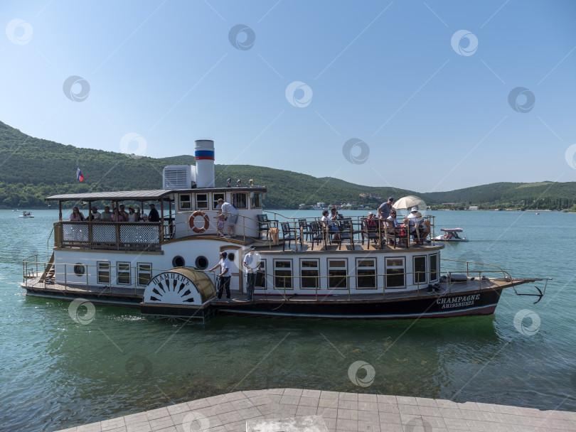Скачать 19 августа 2025 года пассажирский теплоход "Шампань" причаливает к берегу озера Абрау-Дюрсо, окруженного спокойной водой и живописным ландшафтом фотосток Ozero
