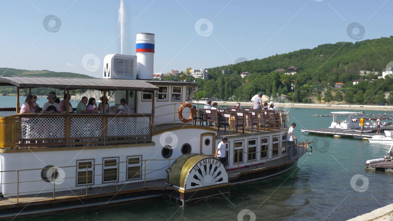 Скачать 19 августа 2025 года пассажирский теплоход "Шампань" причаливает к берегу озера Абрау-Дюрсо, окруженного спокойной водой и живописным ландшафтом фотосток Ozero