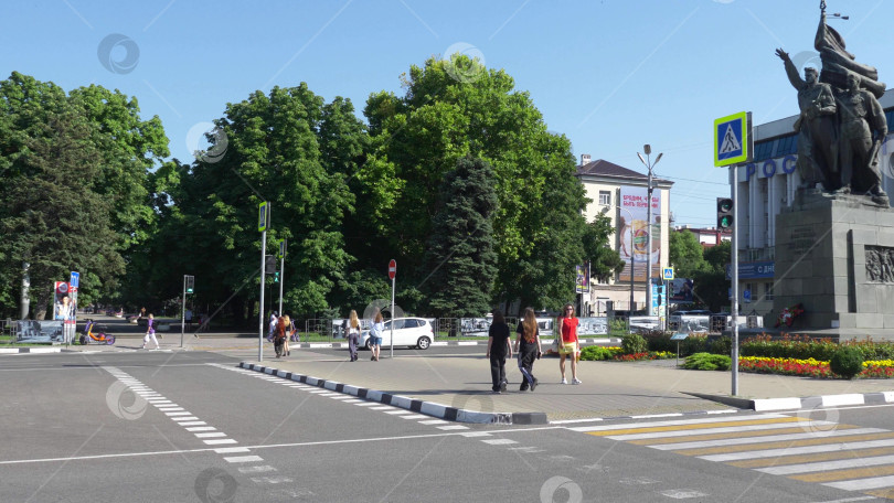 Скачать 12 августа 2025 года: Площадь Свободы в Новороссийске, Россия, центральное общественное пространство, где люди передвигаются по городу в лучах летнего солнца. фотосток Ozero