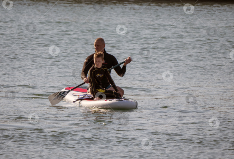 Скачать 12 августа 2025 года: Отец и сын гребут на стоячей доске в море. фотосток Ozero