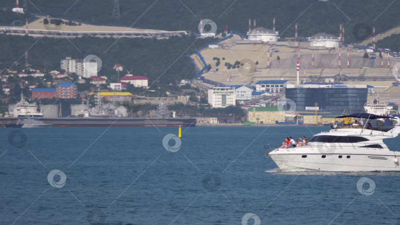 Скачать 12 августа 2025 года: Белая моторная лодка возле порта Новороссийск, Россия, с отдыхающими на борту людьми. фотосток Ozero