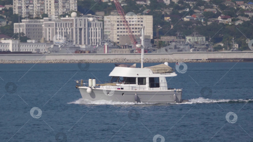 Скачать 12 августа 2025 года: Белая моторная лодка возле порта Новороссийск, Россия, с отдыхающими на борту людьми. фотосток Ozero