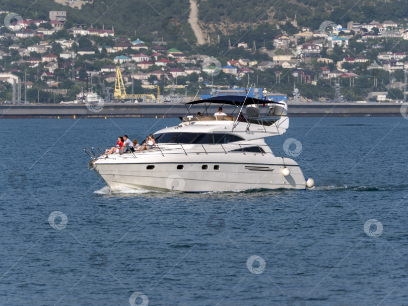 Скачать 12 августа 2025 года: Белая моторная лодка возле порта Новороссийск, Россия, с отдыхающими на борту людьми. фотосток Ozero