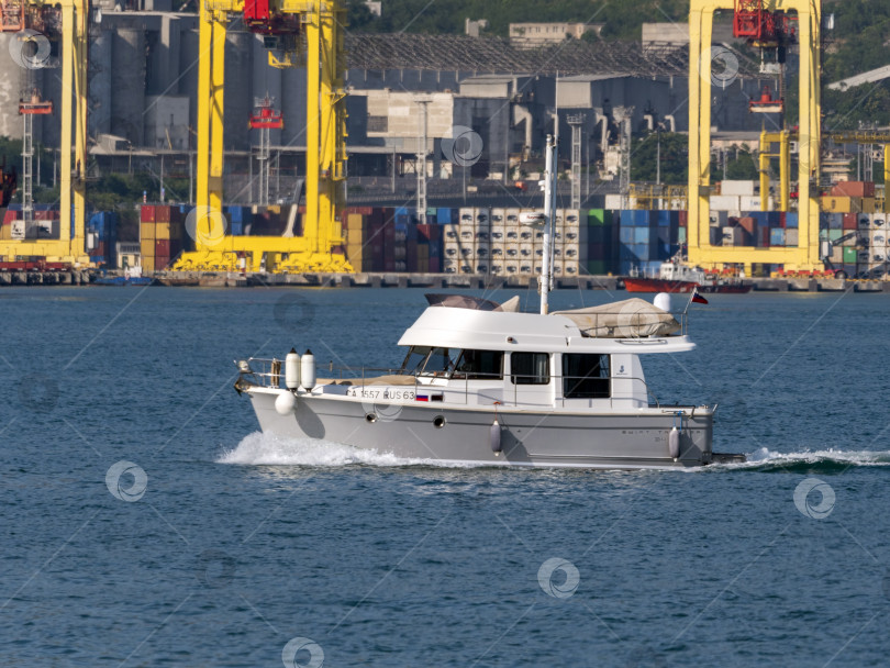 Скачать 12 августа 2025 года: Белая моторная лодка возле порта Новороссийск, Россия, с отдыхающими на борту людьми. фотосток Ozero