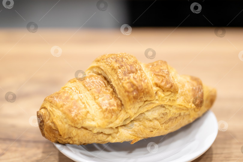 Скачать Вкусный слоеный круассан с хрустящей корочкой, приготовленный на деревянной поверхности под утренним солнцем фотосток Ozero