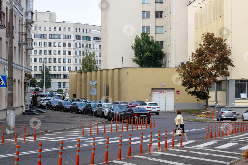 Скачать Беларусь, Минск - 22.09.2024: Одинокий пешеход, идущий по тихим городским улицам с припаркованными автомобилями и нейтральными зданиями фотосток Ozero
