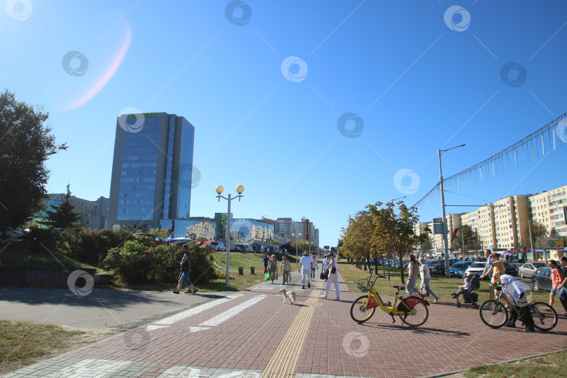 Скачать Беларусь, Минск - 22.09.2024: Люди гуляют и катаются на велосипедах под ясным небом в шумном городе, где царит расслабляющая атмосфера фотосток Ozero