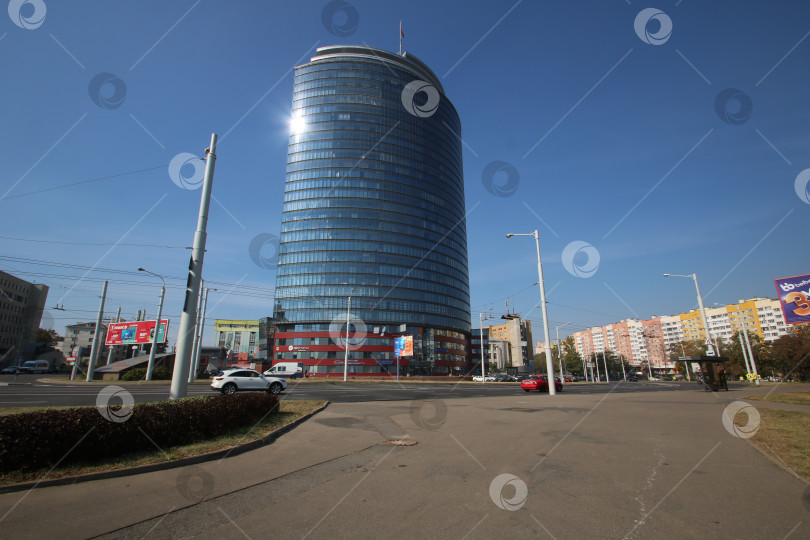 Скачать Беларусь, Минск - 22.09.2024: Обзор современного городского пейзажа. Современное стеклянное здание возвышается вдоль оживленного городского бульвара фотосток Ozero